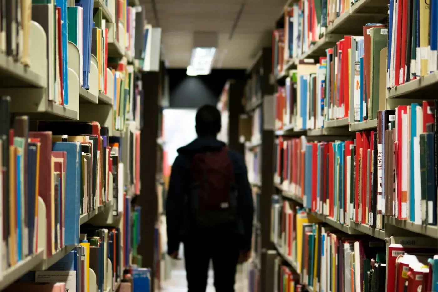 A student walking between tall library shelves